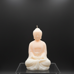 A light peach and cream colored meditating Buddha soy wax scented candle on a clear acrylic stand.