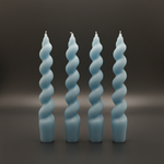 Set of four light blue spiral taper candles standing upright on a dark surface, front view.