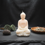 A light pink meditating Buddha soy wax scented candle with lotus pods and tea leaves.