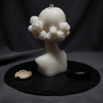 The Bloom Maiden Bust Candle in white, featuring a delicate rose-adorned head and bust, presented on a dark slate.