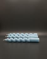 Set of four light blue spiral taper candles arranged horizontally on a dark gray surface.