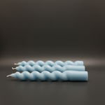 Set of four light blue spiral taper candles arranged horizontally on a dark gray surface.