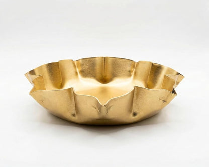 A gold-tone lotus-shaped urli bowl with a ruffled edge, presented from a front-facing perspective.