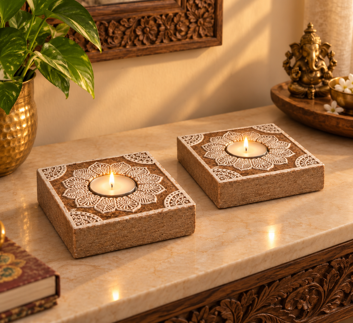 Two lit mandala tealight holders on a marble console beside a brass Ganesha and a money plant