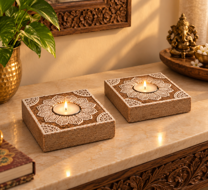 Two lit mandala tealight holders on a marble console beside a brass Ganesha and a money plant