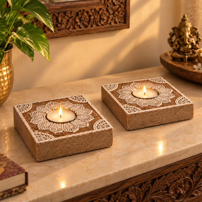 Two lit mandala tealight holders on a marble console beside a brass Ganesha and a money plant