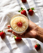 Sun-Kissed Daisy clear glass soy wax candle with a floral design, held by a hand surrounded by strawberries.