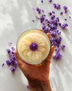 Top view of a Sun-Kissed Daisy clear glass soy wax candle with a floral design, surrounded by lavender.