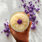 Top view of a Sun-Kissed Daisy clear glass soy wax candle with a floral design, surrounded by lavender.
