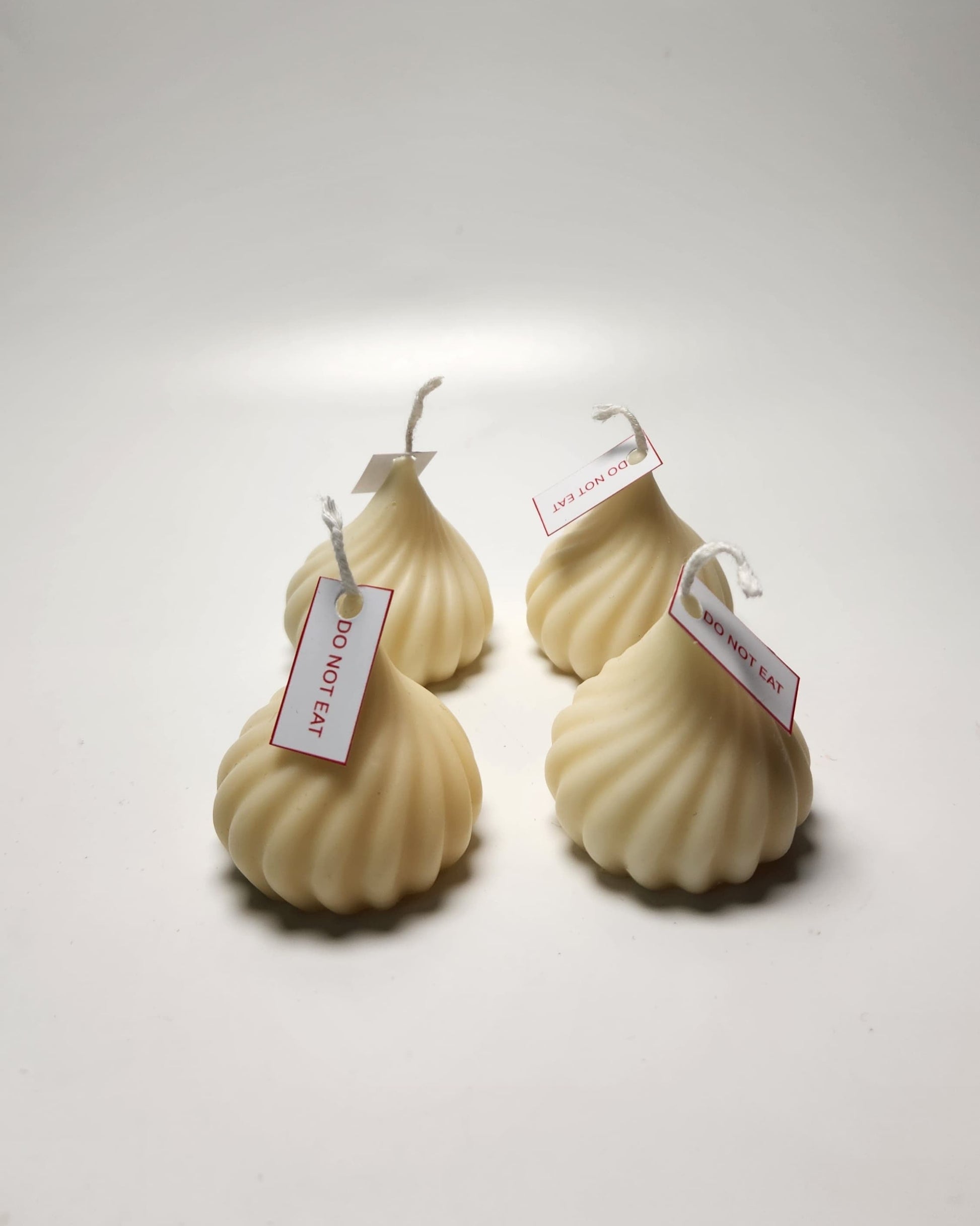 Four modak-shaped candles with tags on a light gray background