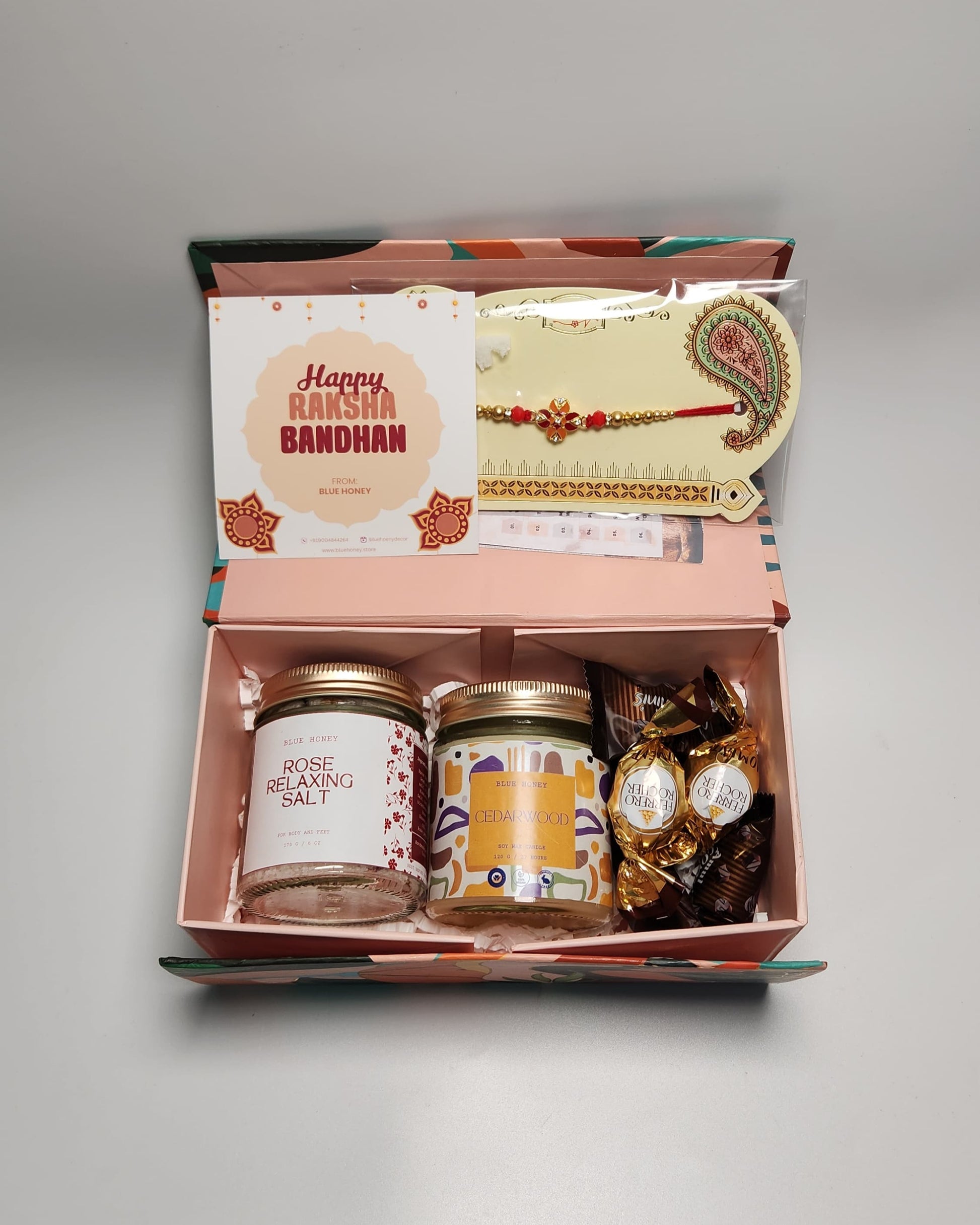 Gift box with candles, rakhi, and card on a gray background