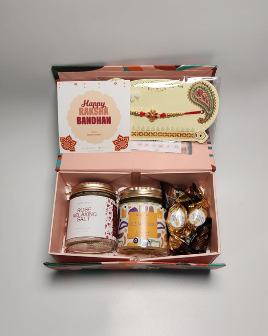 Gift box with candles, rakhi, and card on a gray background