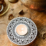 Close-up of a handcrafted white wooden carved tealight holder with a lit candle on a wooden surface.