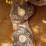 Two handcrafted wooden carved tealight holders with intricate white patterns, lit with candles, on a burlap background.