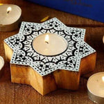Handcrafted wooden star tealight holder with intricate carved details, lit by a candle, on a wooden surface.