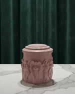 Pink Jesmonite Renaissance Relic Scrolled candle vessel with angel carvings on a marble surface.