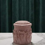 Pink Jesmonite Renaissance Relic Scrolled candle vessel with angel carvings on a marble surface.