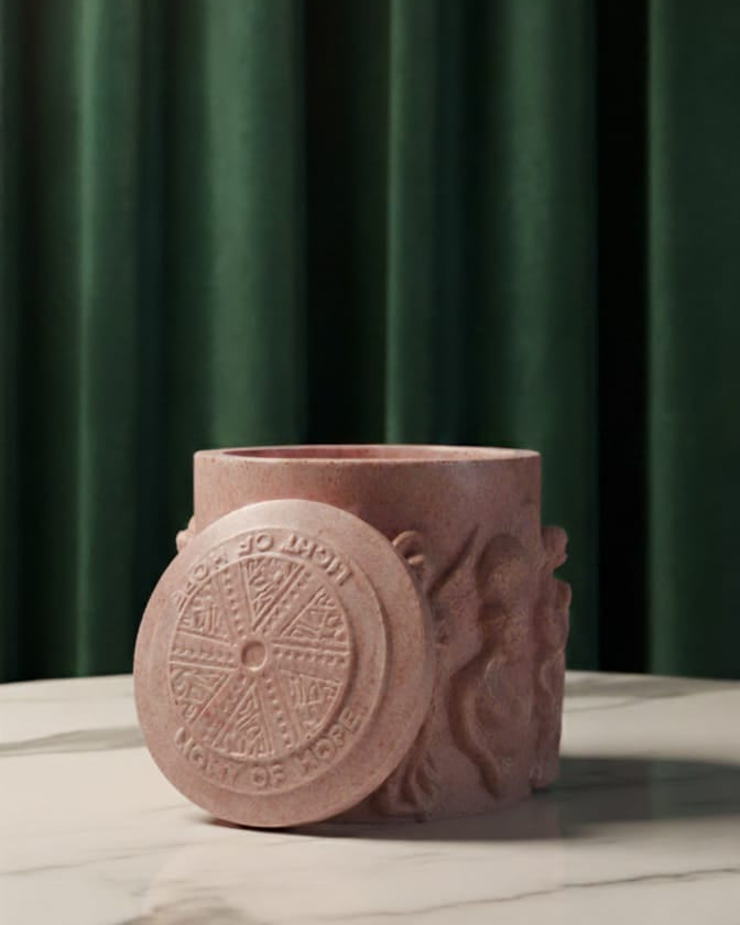 Pink ceramic container with decorative design on a marble surface against a green curtain background