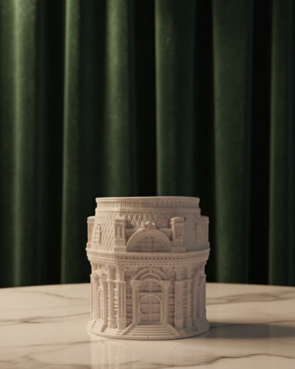 Decorative stone tower candle jar on a marble surface with a green curtain background