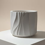 Modern Wave Vessel scented Jesmonite candle in a light grey, textured finish, displayed from the front.