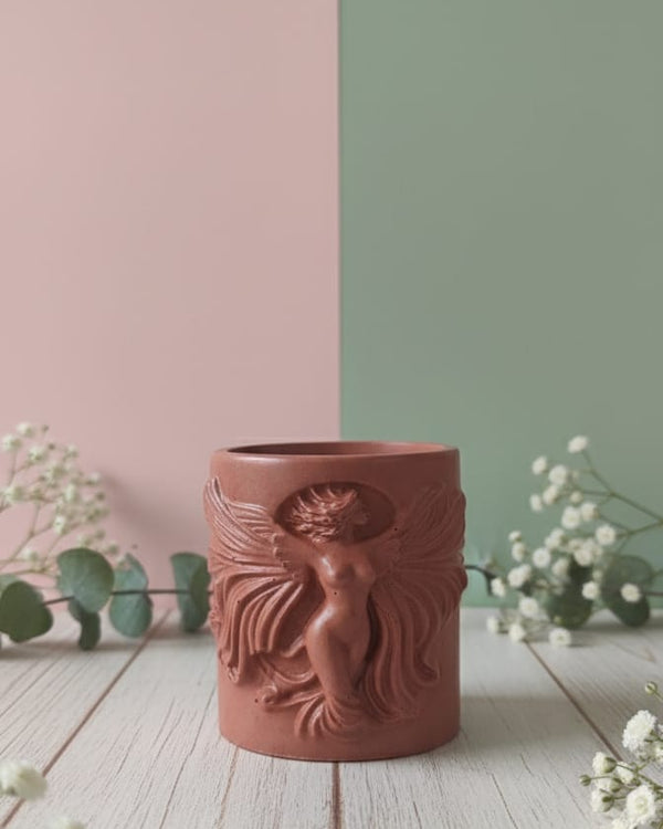 The Risen Phoenix Relief Jesmonite Candle, a terracotta-colored candle with a detailed phoenix design, displayed on a wooden surface.