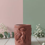 The Risen Phoenix Relief Jesmonite Candle, a terracotta-colored candle with a detailed phoenix design, displayed on a wooden surface.