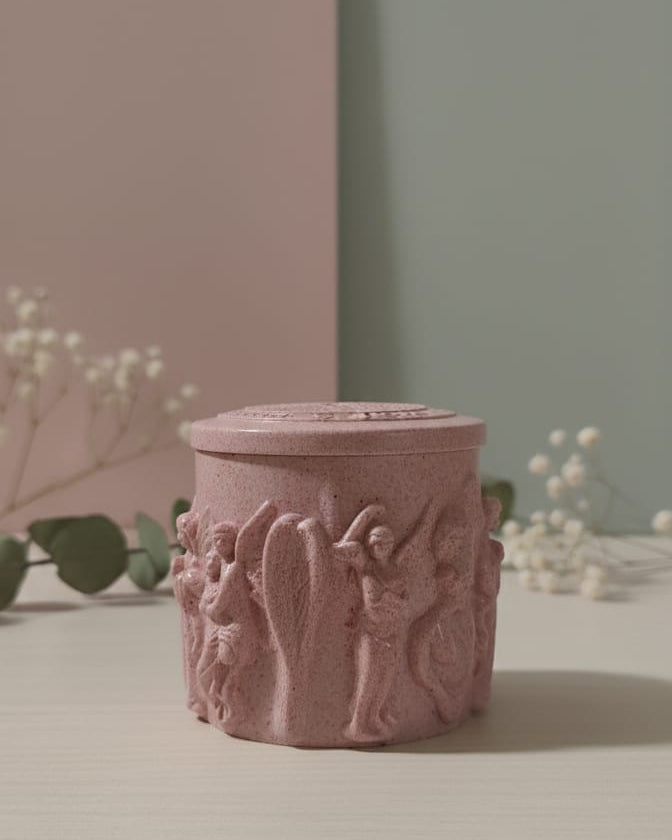 Pink textured candle holder on a light surface with white flowers and green leaves in the background
