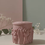 Pink Jesmonite Renaissance Relic Scrolled candle vessel with intricate relief carvings, displayed front and center.