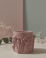 Pink Jesmonite Renaissance Relic candle vessel with scrolled angel details, displayed on a table.