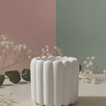 A white scalloped flute Jesmonite scented candle sits on a light-colored surface with delicate white flowers.