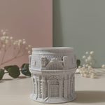 The Grand Pavilion Architectural Jesmonite Candle Jar, a detailed grey miniature building, displayed on a table.
