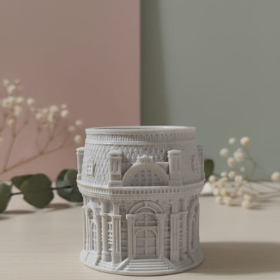 The Grand Pavilion Architectural Jesmonite Candle Jar, a detailed grey miniature building, displayed on a table.