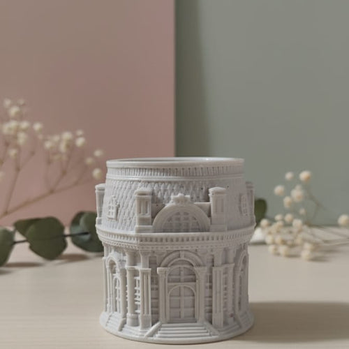 The Grand Pavilion Architectural Jesmonite Candle Jar, a detailed grey miniature building, displayed on a table.