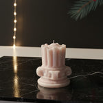A pink mini Corinthian pillar candle with intricate detailing, displayed on a black marble surface.