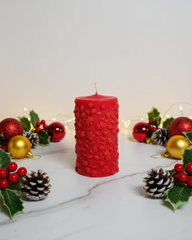 Red textured candle surrounded by Christmas decorations on a white surface
