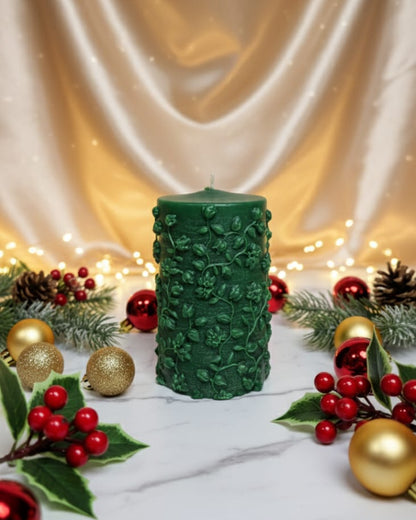 Green textured candle with Christmas decorations on a white surface