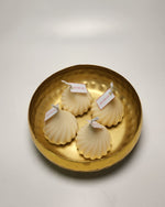 Four white modak-shaped scented candles with 'DO NOT EAT' tags, arranged in a textured gold bowl.
