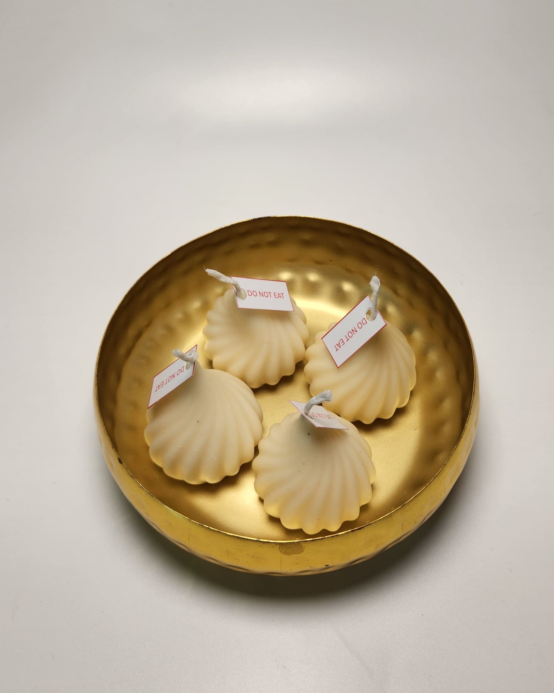 Four white modak candles with labels on a gold dish against a white background