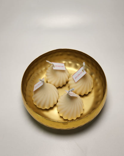Four white modak candles with labels on a gold dish against a white background