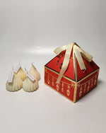 Red gift box with a cream-colored ribbon tied around it, next to three modak-shaped candles.