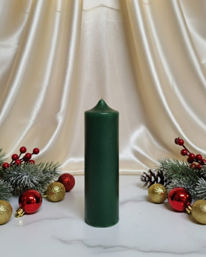 Green candle on a white surface with Christmas decorations and string lights in the background.