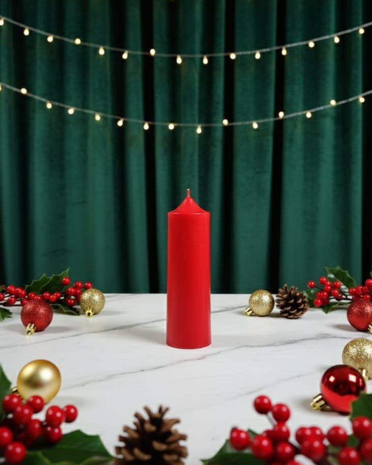 Red candle on a white surface with Christmas decorations and string lights against a green curtain.