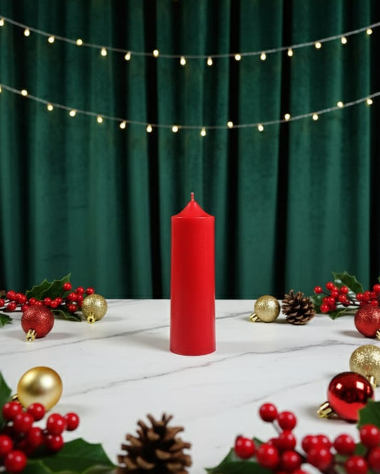 Red candle on a white surface with Christmas decorations and string lights against a green curtain.