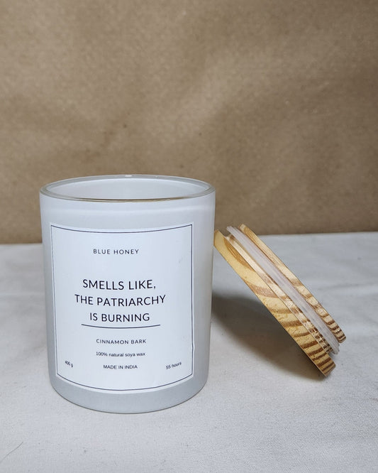White matte glass candle jar with wooden lid label reads "Smells like the patriarchy is burning"