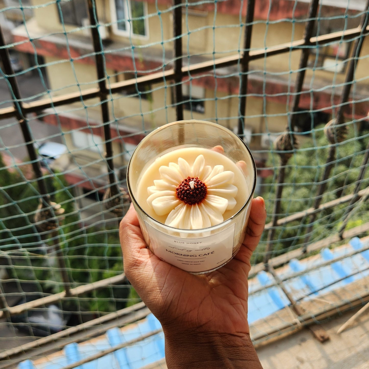 brown bud daisy flower candle inside a clear jar in palm of a female, outside the window.