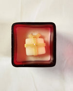 Top view of a red glass jar Christmas candle featuring a white gift-shaped candle with gold ribbon detail.