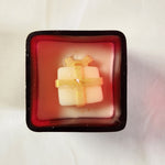 Top view of a red glass jar Christmas candle featuring a white gift-shaped candle with gold ribbon detail.