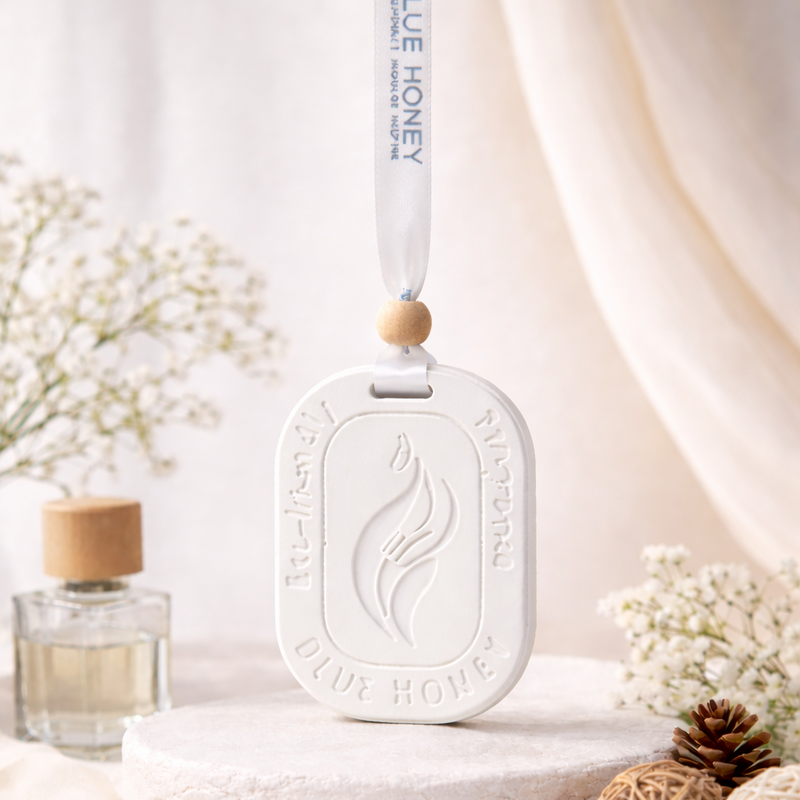 White oval car aroma tag diffuser with 'Blue Honey' branding, hanging from a ribbon.