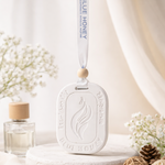 White oval car aroma tag diffuser with 'Blue Honey' text and flame design, hanging from a ribbon.