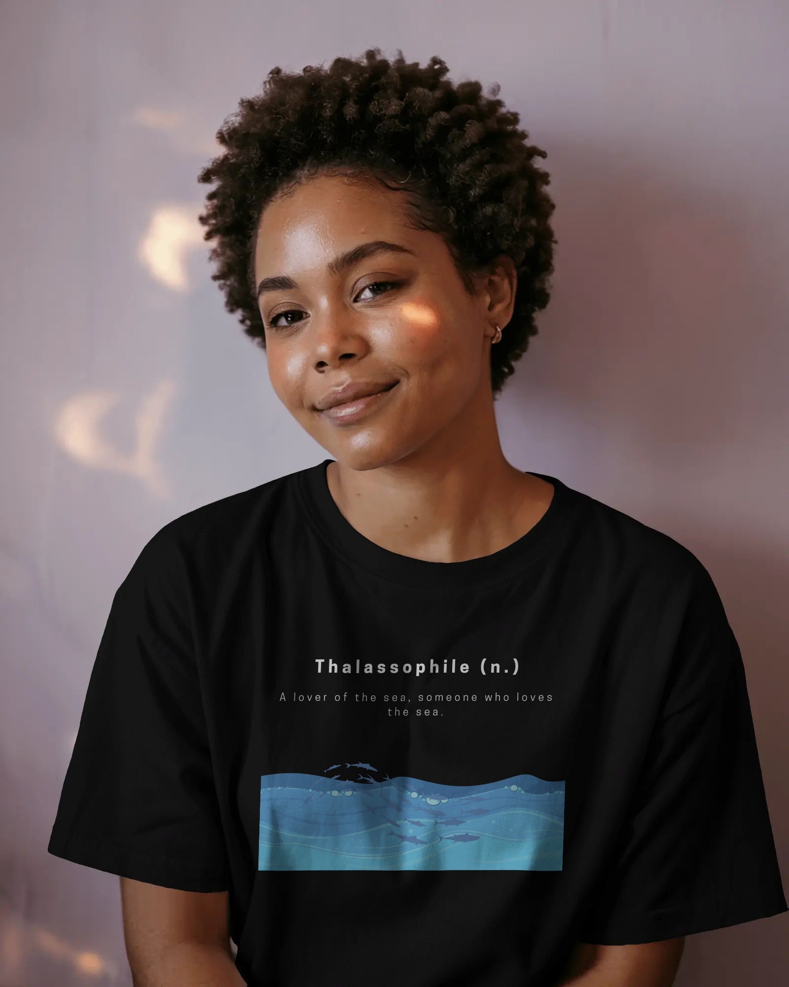 a black female model sitting and smiling wearing an oversized Thalassophile black tshirt 